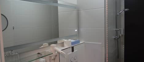 Un baño moderno con cabina de ducha de vidrio, inodoro blanco y espejo sobre el lavabo.