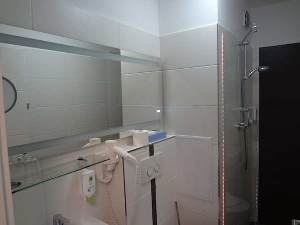 Un baño moderno con cabina de ducha de vidrio, inodoro blanco y espejo sobre el lavabo.