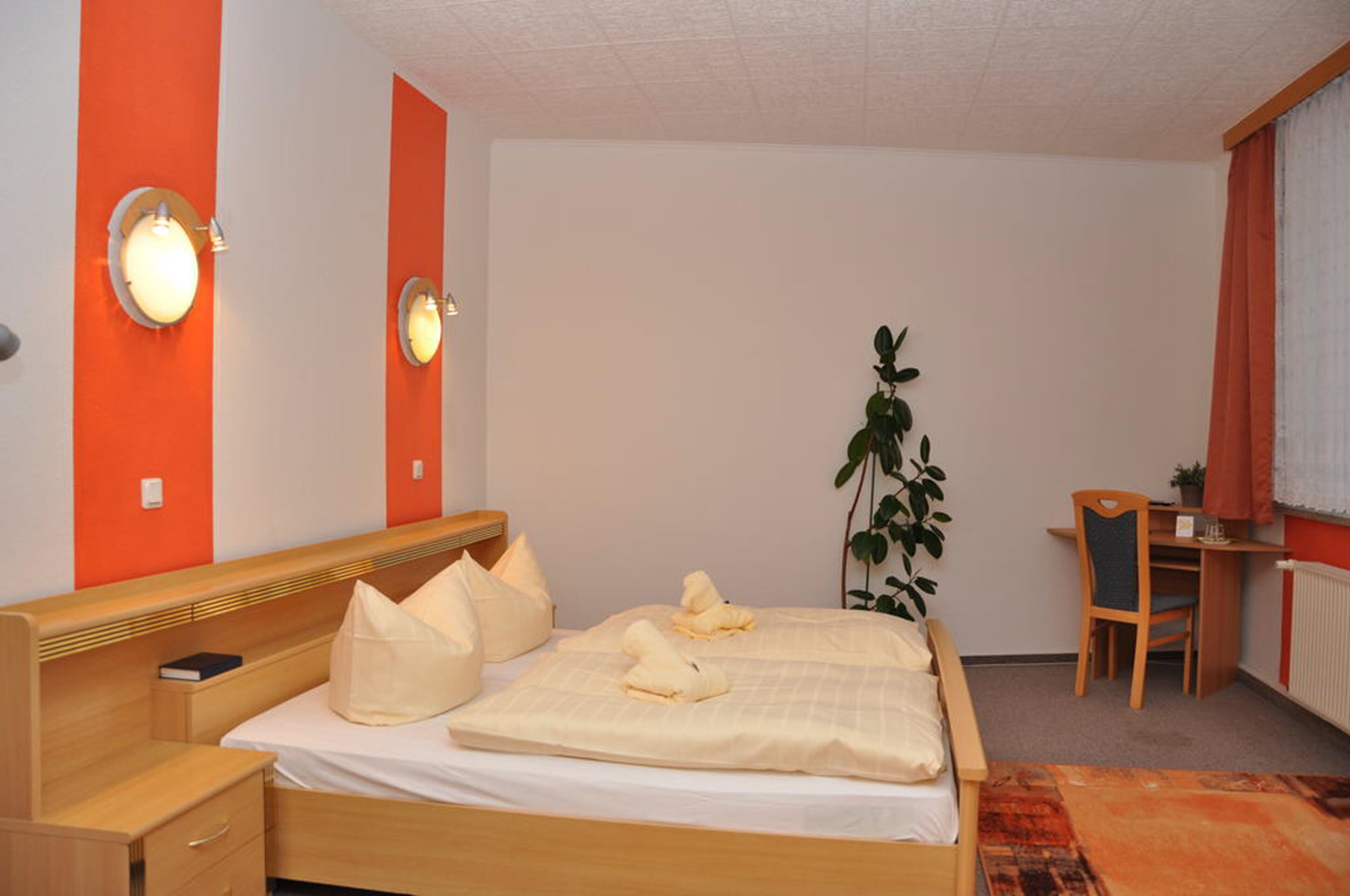 Ein Hotelzimmer mit Bett, Nachttisch, Lampe und Schreibtisch mit Stuhl.