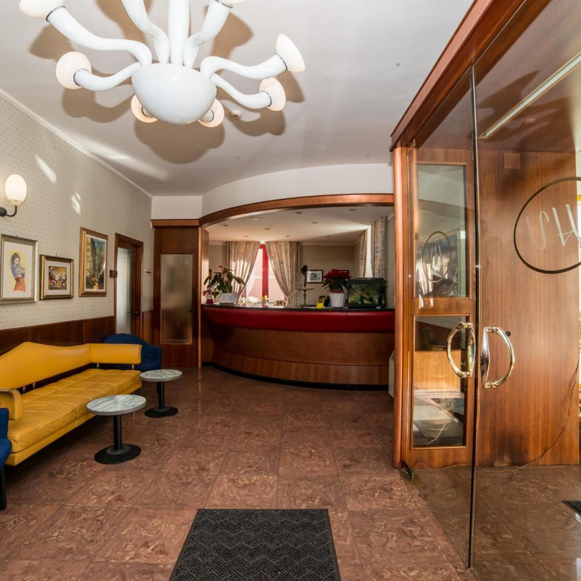 A lobby with a reception desk, seating area, and a modern chandelier.