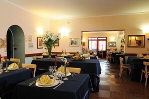 A dining area with tables set for multiple guests, featuring a checkered floor pattern and warm lighting. - Hotel Victoria (Rivisondoli)
