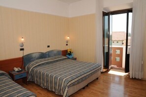 A hotel room with two beds, a wooden floor, a balcony with a view, and a nightstand with a phone and flowers. - Hotel Victoria (Rivisondoli)