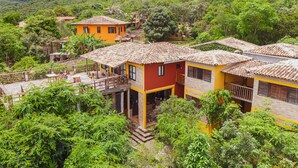 A multi-story building with a red and yellow facade, multiple balconies, and a patio area with outdoor seating. - Pousada Alto do Cajueiro (Lençóis)