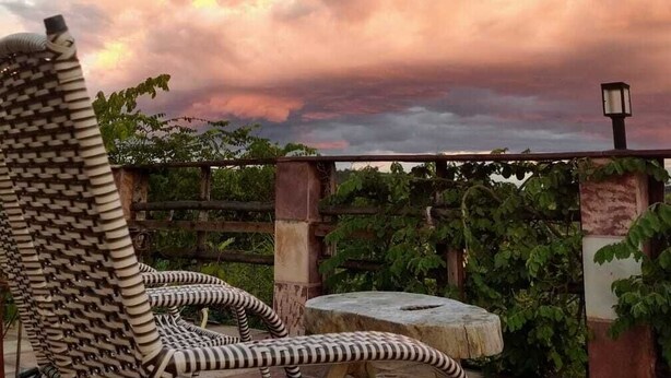 A wicker chair and a small table in an outdoor patio area with a view of the sky and clouds. - Pousada Alto do Cajueiro (Lençóis)