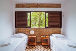 Quarto com duas camas, parede de tijolos e janela com persianas.