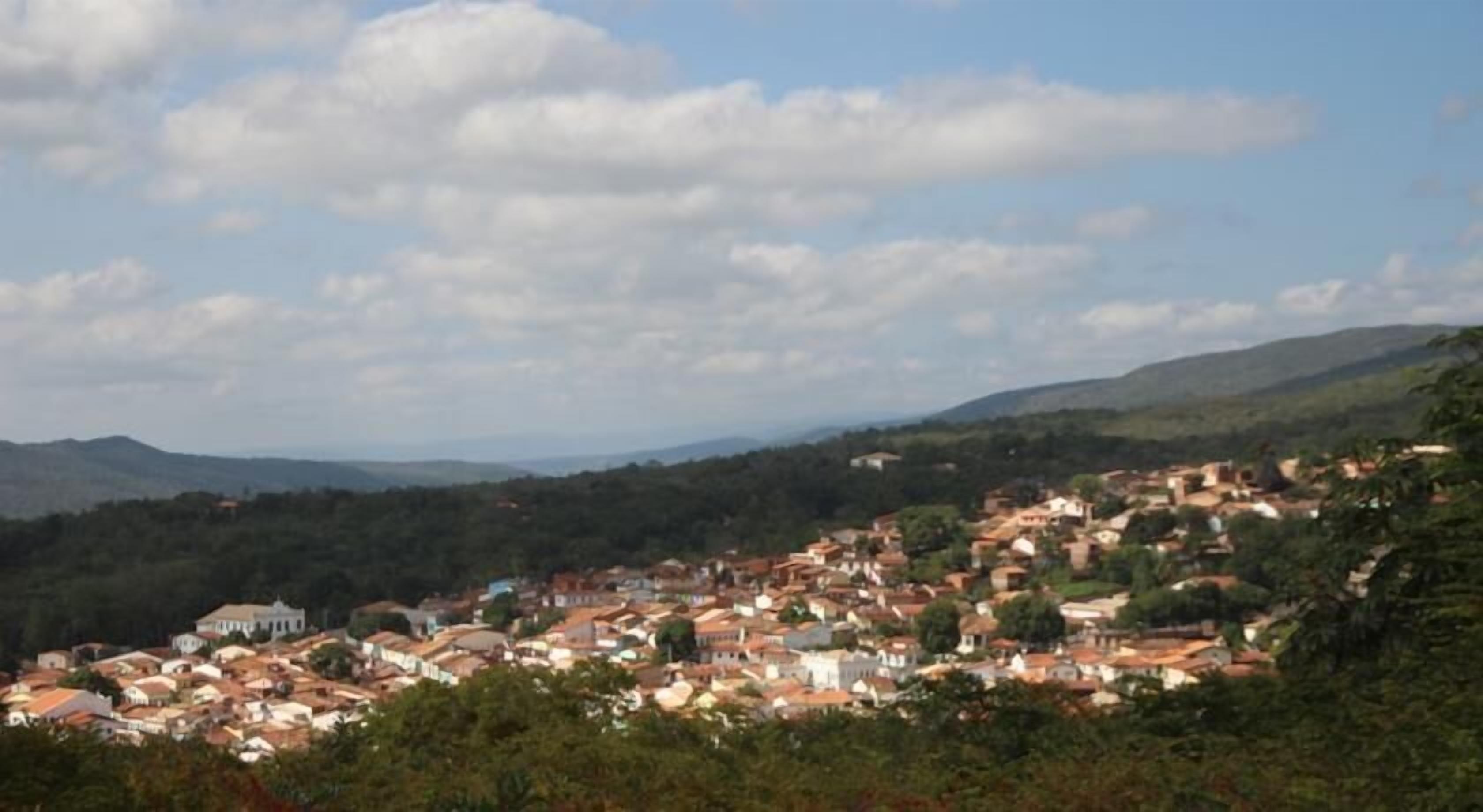 A town nestled in a valley with a mix of traditional and modern buildings, surrounded by hills and greenery.