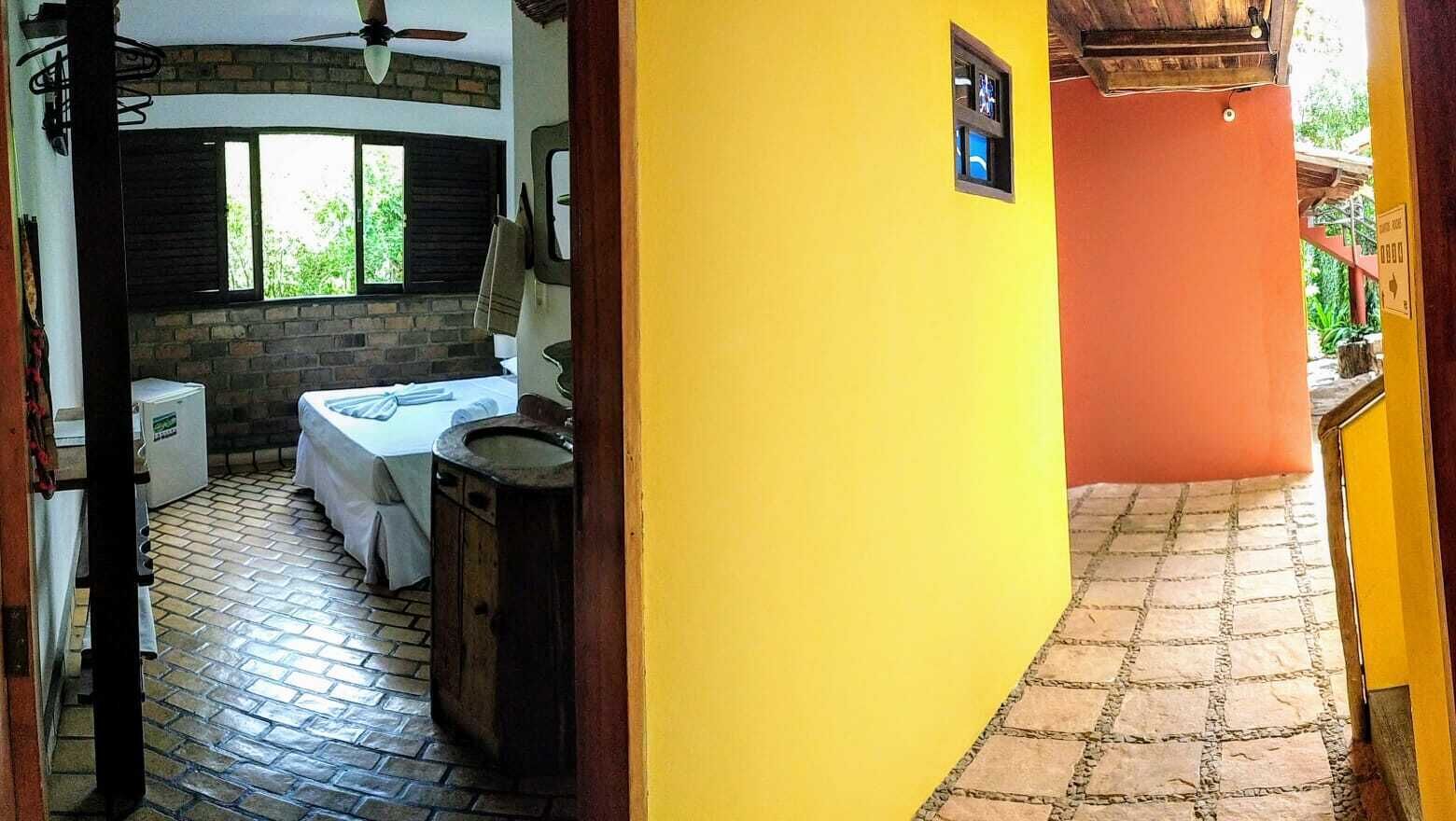 A room with a brick fireplace, a bed, a small table, and a window with a view of greenery.