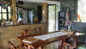A rustic dining area with a long wooden table, benches, and a brick wall. - Pousada Alto do Cajueiro (Lençóis)