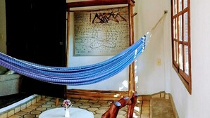 A room with a hammock, a wooden chair, a small table, and a large window. - Pousada Alto do Cajueiro (Lençóis)