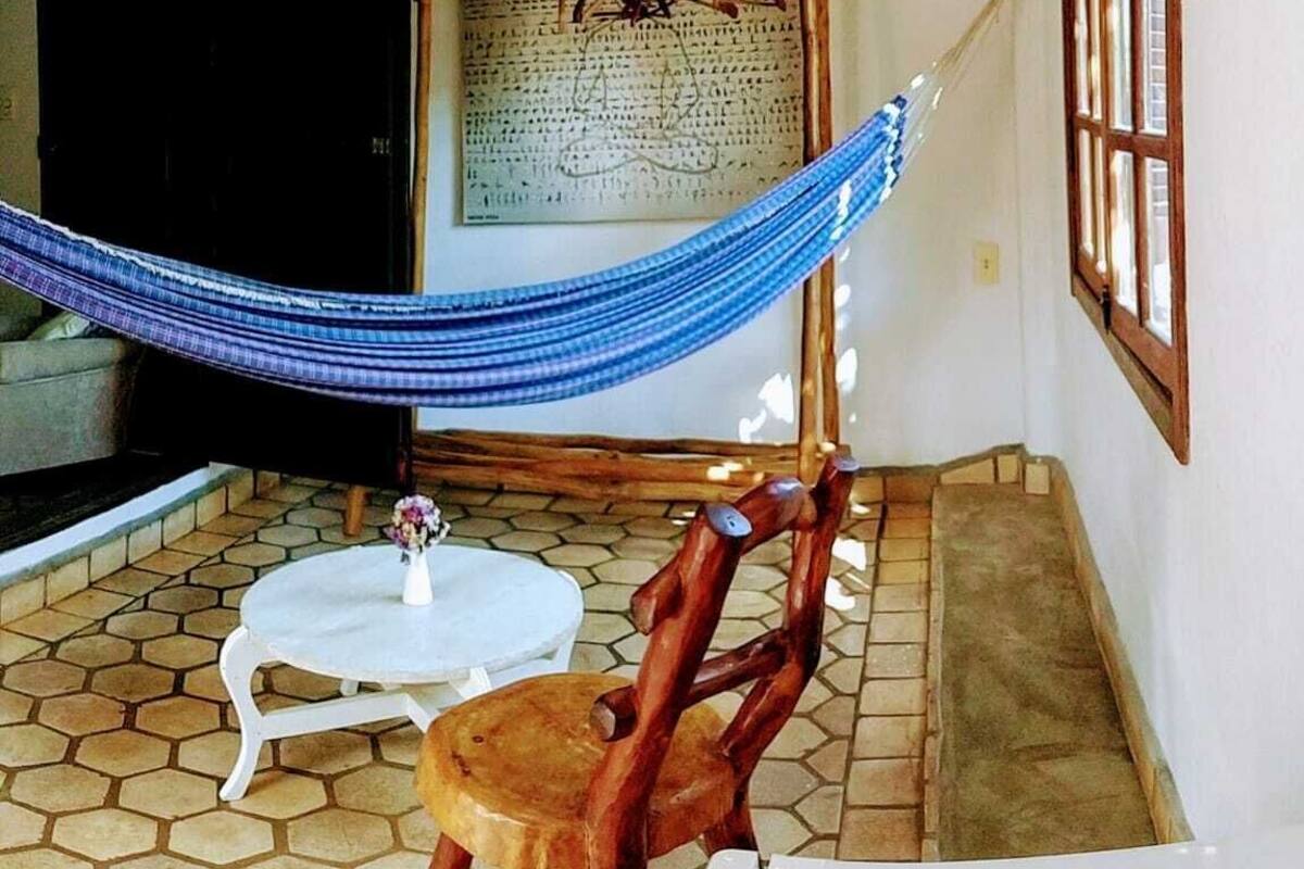 A room with a hammock, a wooden chair, a small table, and a large window.