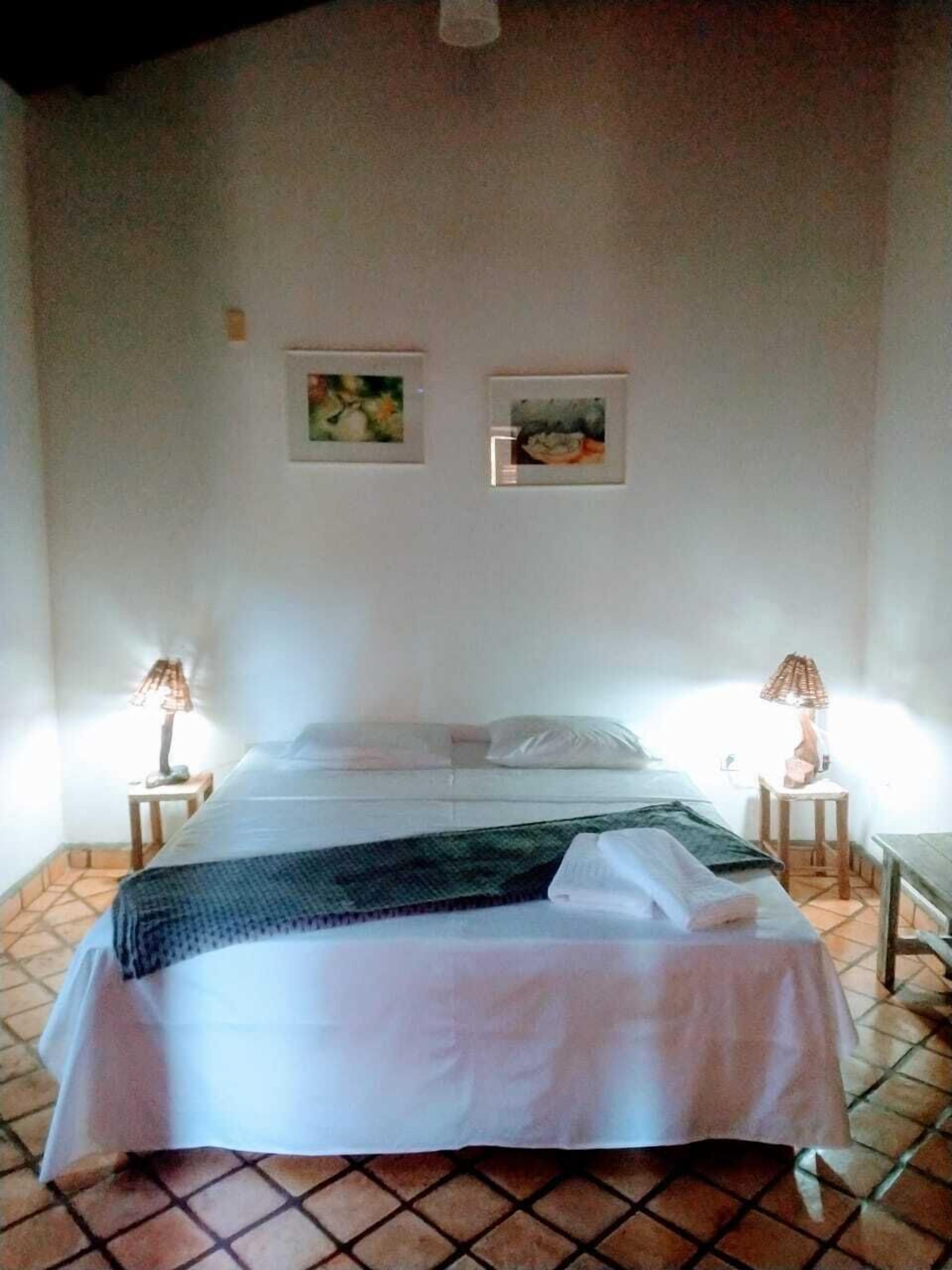 A hotel room with a bed, two bedside lamps, and two framed pictures on the wall.
