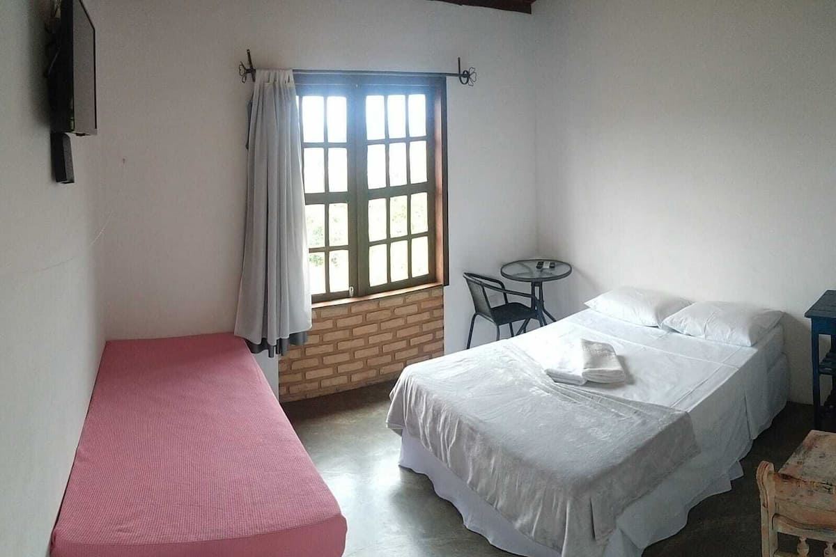 A room with a bed, a small table, a chair, and a window with curtains.