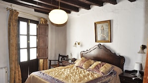 A bedroom with a wooden bed, a nightstand, a lamp, a framed picture on the wall, and a window with curtains. - Casa Rural Las Piedras (Grazalema)