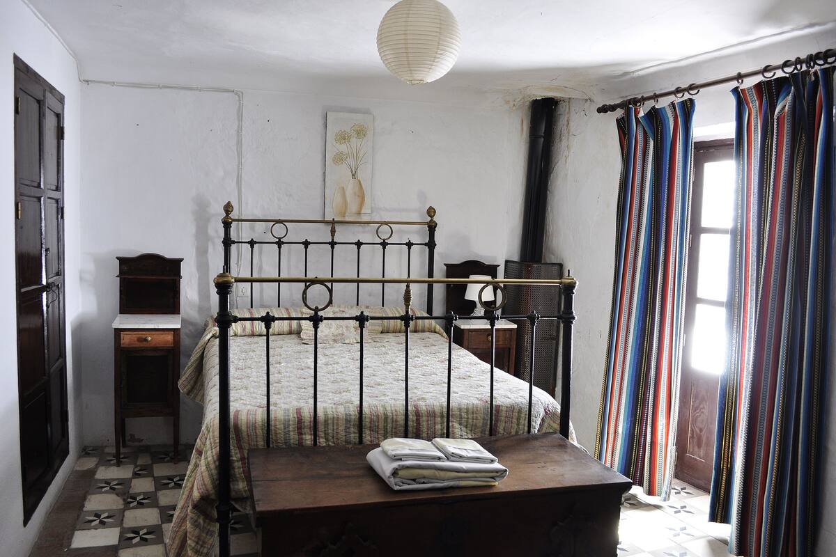 Ein Schlafzimmer mit einem Bett, einem Nachttisch, einer Kommode und einem Fenster mit Vorhängen.