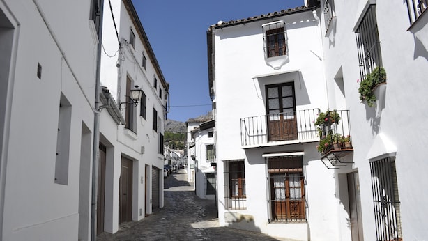 A narrow cobblestone street flanked by white buildings with balconies and windows. - Casa Rural Las Piedras (Grazalema)