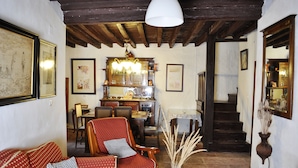 A cozy living room with a red sofa, wooden chairs, a dining table, and a staircase leading to another level. - Casa Rural Las Piedras (Grazalema)
