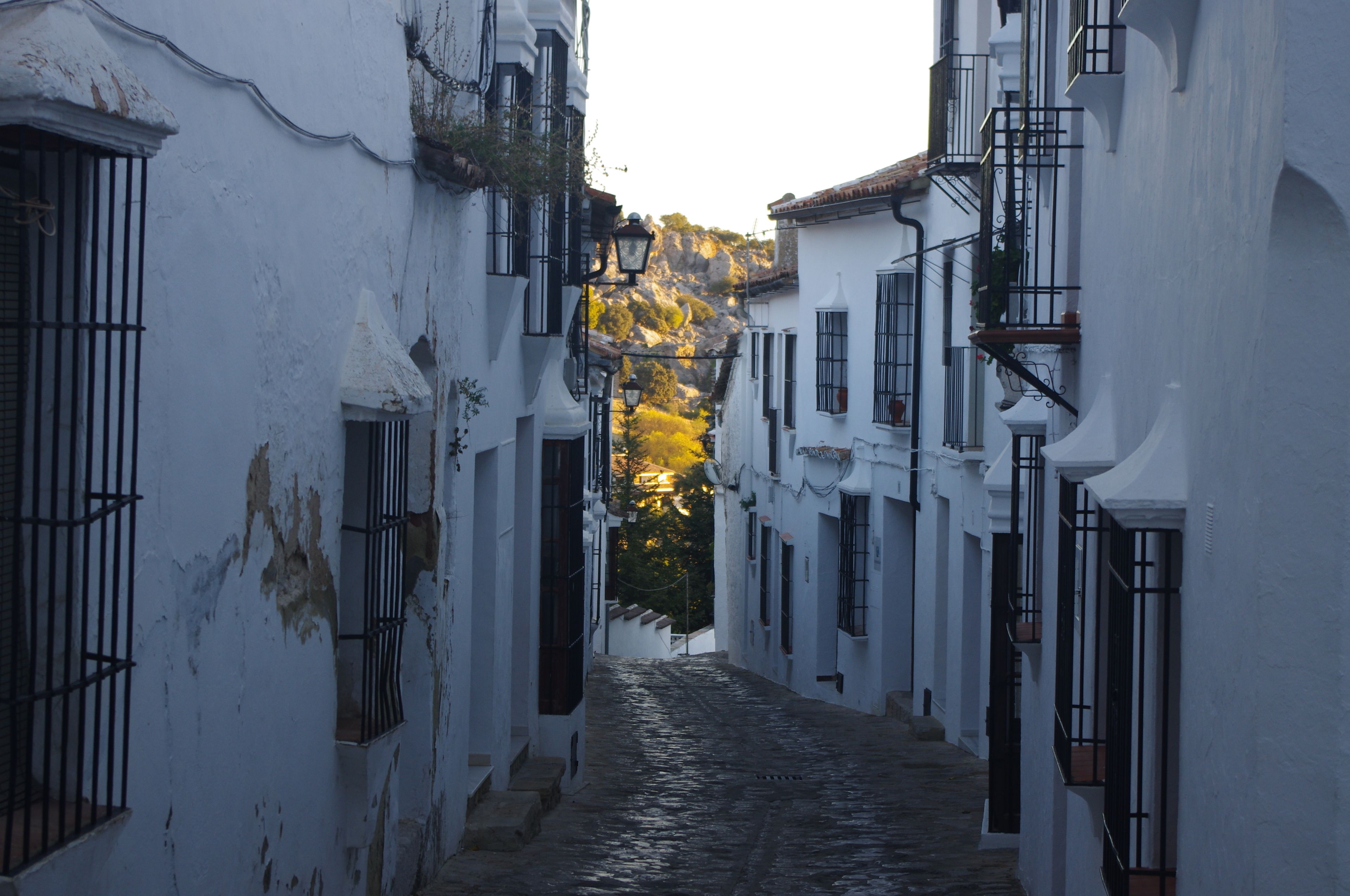 Una estrecha calle adoquinada bordeada por edificios blancos con rejas y balcones.