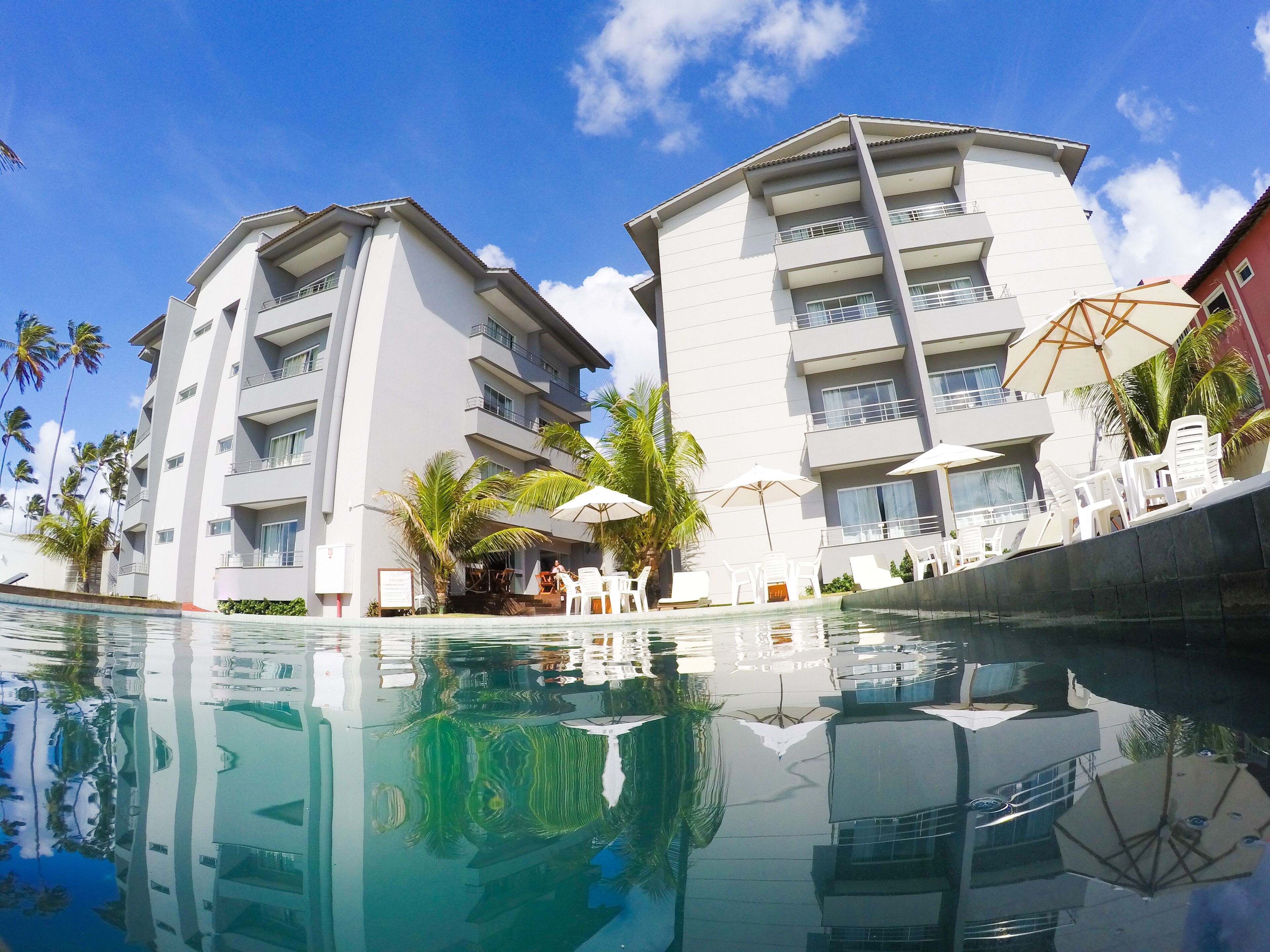 A modern hotel with a swimming pool, multiple balconies, and outdoor seating areas.