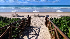 A beach path leading to the ocean with beach chairs and umbrellas. - Hotel Pousada Butias   (Ipojuca)