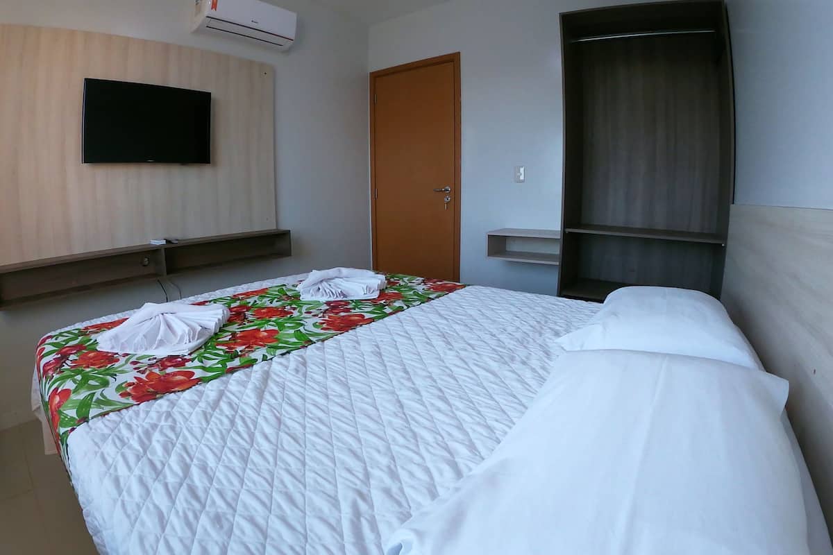 A hotel room with a bed, a TV mounted on the wall, a wooden wardrobe, and a door.