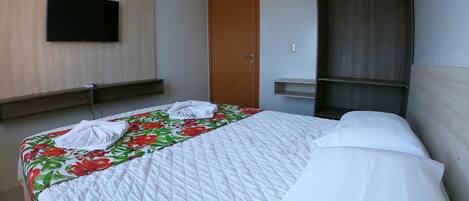 A hotel room with a bed, a TV mounted on the wall, a wooden wardrobe, and a door.