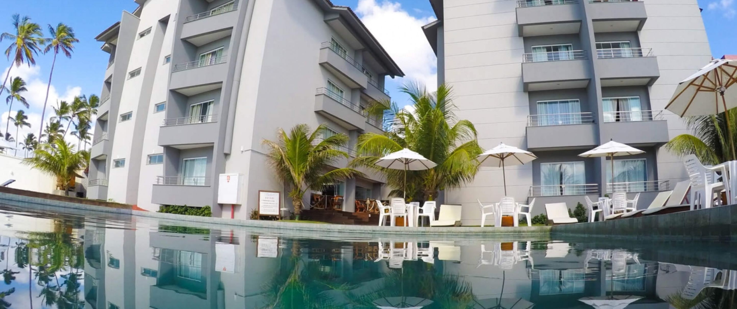 A modern hotel with a swimming pool, multiple balconies, and outdoor seating areas with umbrellas.