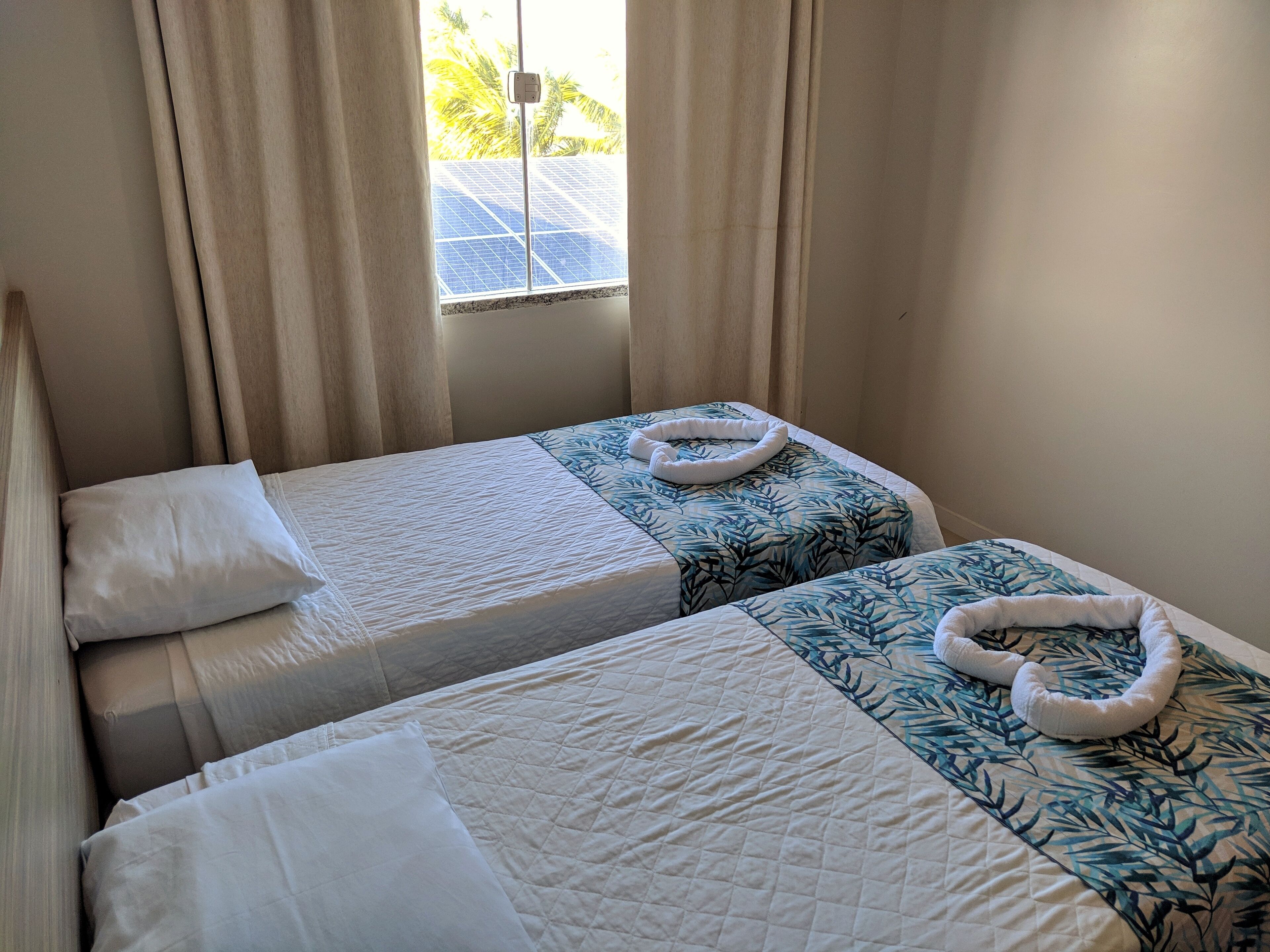 A hotel room with two beds, each with a white quilted bedspread and a matching pillow. There is a window with curtains, and a towel is placed on one of the beds.