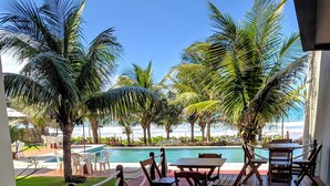 A wooden deck with tables and chairs, overlooking a pool and palm trees. - Hotel Pousada Butias   (Ipojuca)