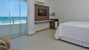 A hotel room with a bed, a desk, a chair, and a large window offering a view of the beach. - Hotel Pousada Butias   (Ipojuca)