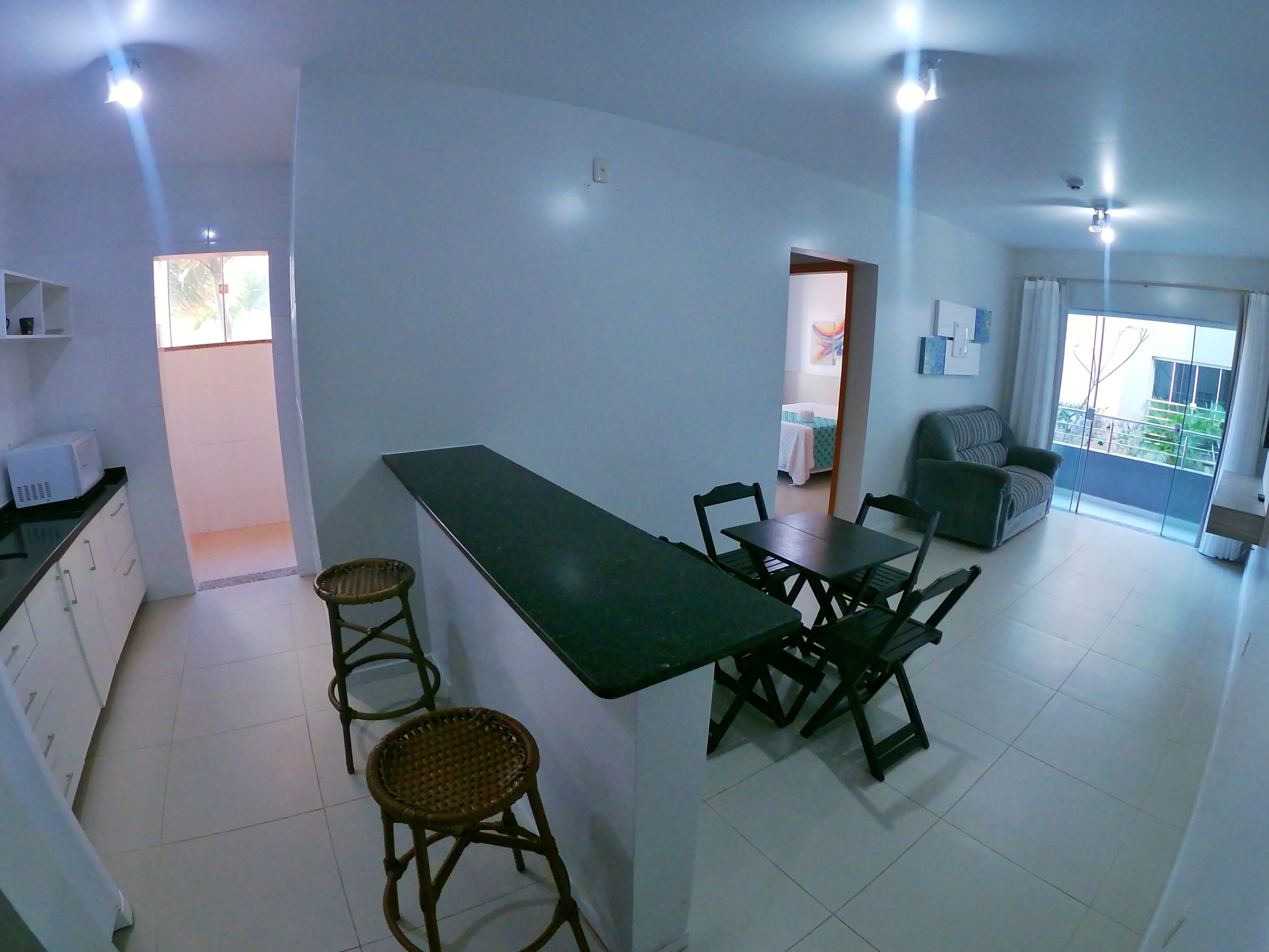 A modern kitchen with a dining area, a small living space, and a balcony with a view.