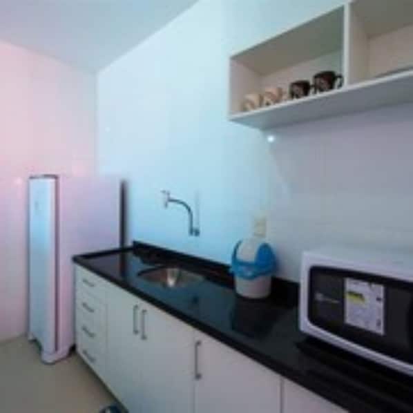 Una cocina compacta con refrigerador, microondas y lavamanos.
