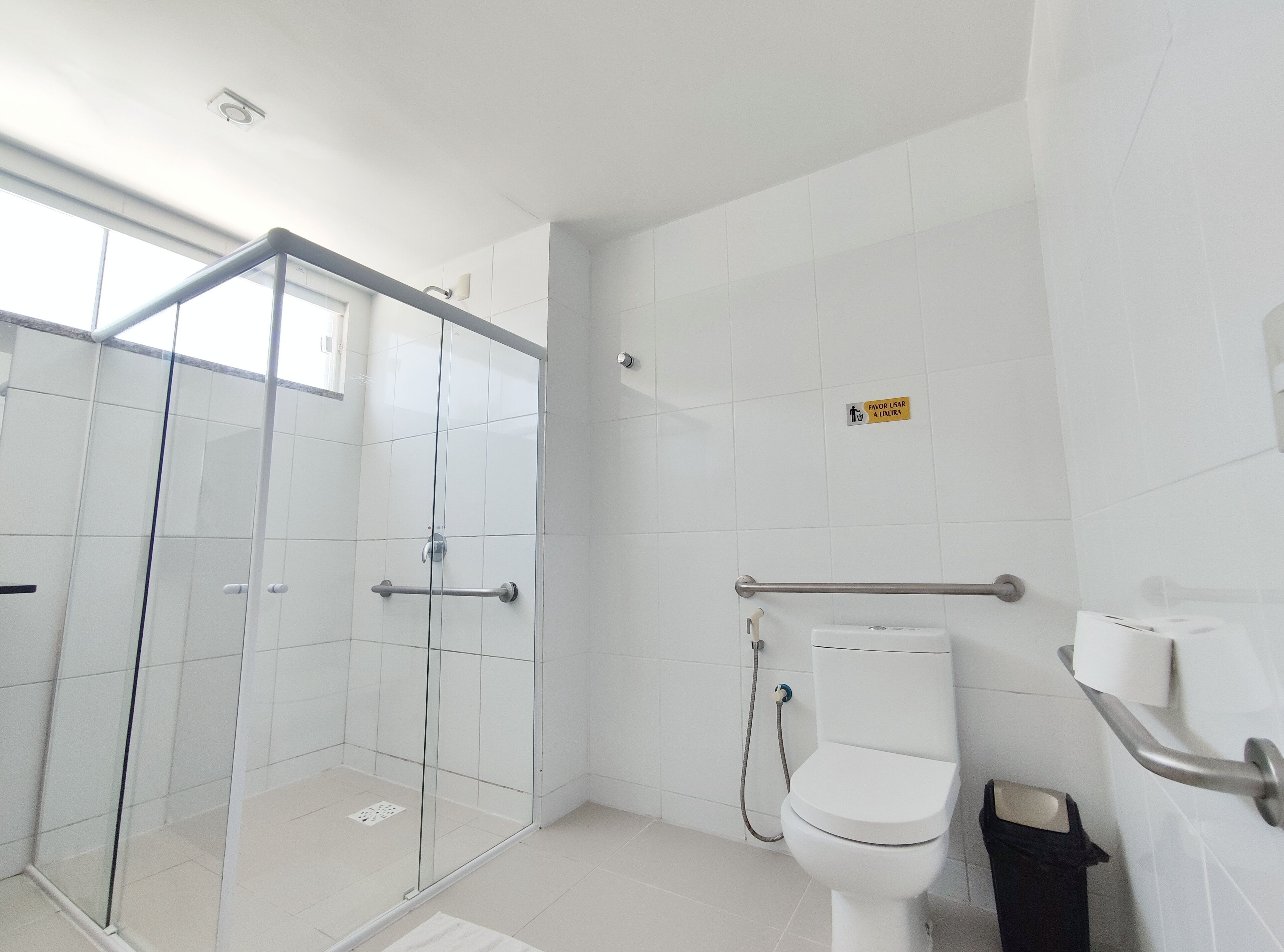 Un bagno moderno con box doccia in vetro, un water con mancorrente e un cestino.