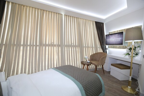 A hotel room with a bed, a desk, a chair, a TV, and a lamp. - Elips Royal Hotel & Spa (Antalya)