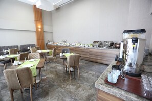 Un restaurante con varias mesas, sillas y una zona de bufé con diversos alimentos y una máquina de café.