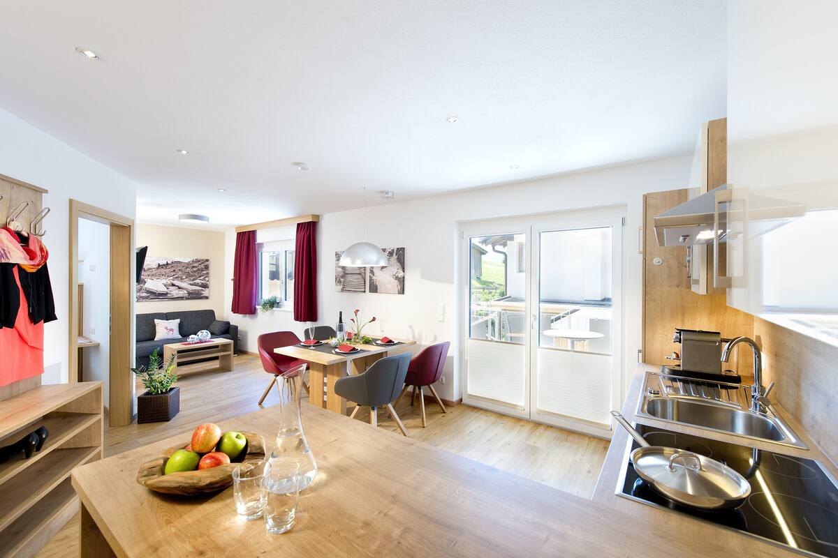 A modern kitchen with a built-in stove, a dining area with a wooden table and chairs, and a living area with a sofa and a coffee table.