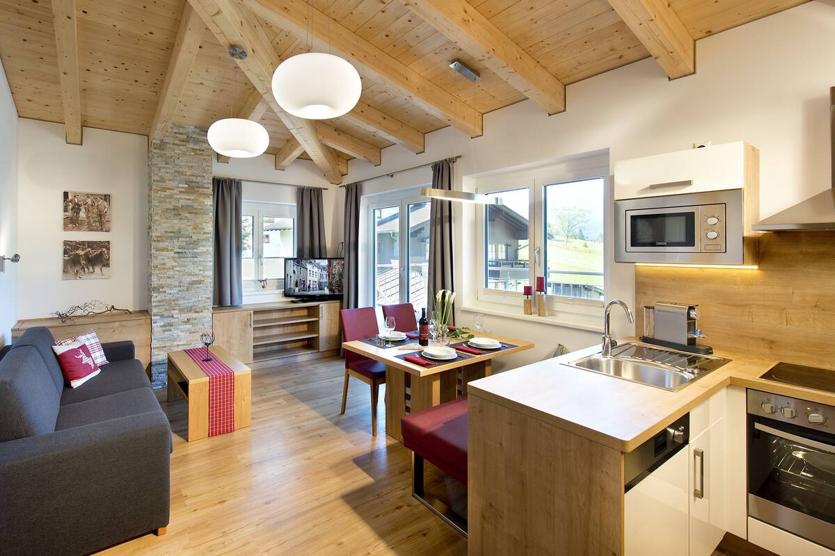 A modern kitchen with wooden beams, a dining area, and a cozy living space with a sofa and a television.