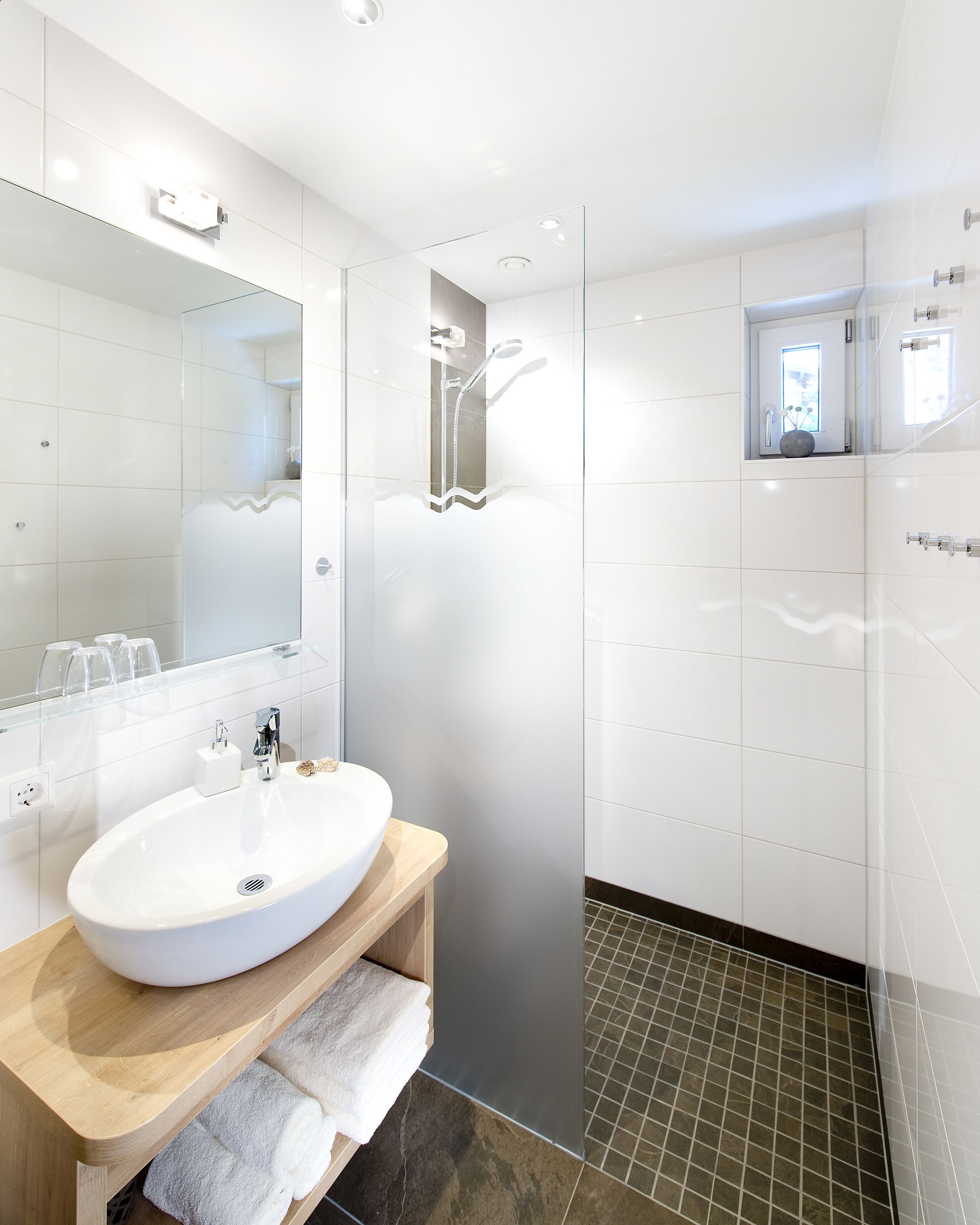 A modern bathroom with a white sink, a glass shower enclosure, and a small window.
