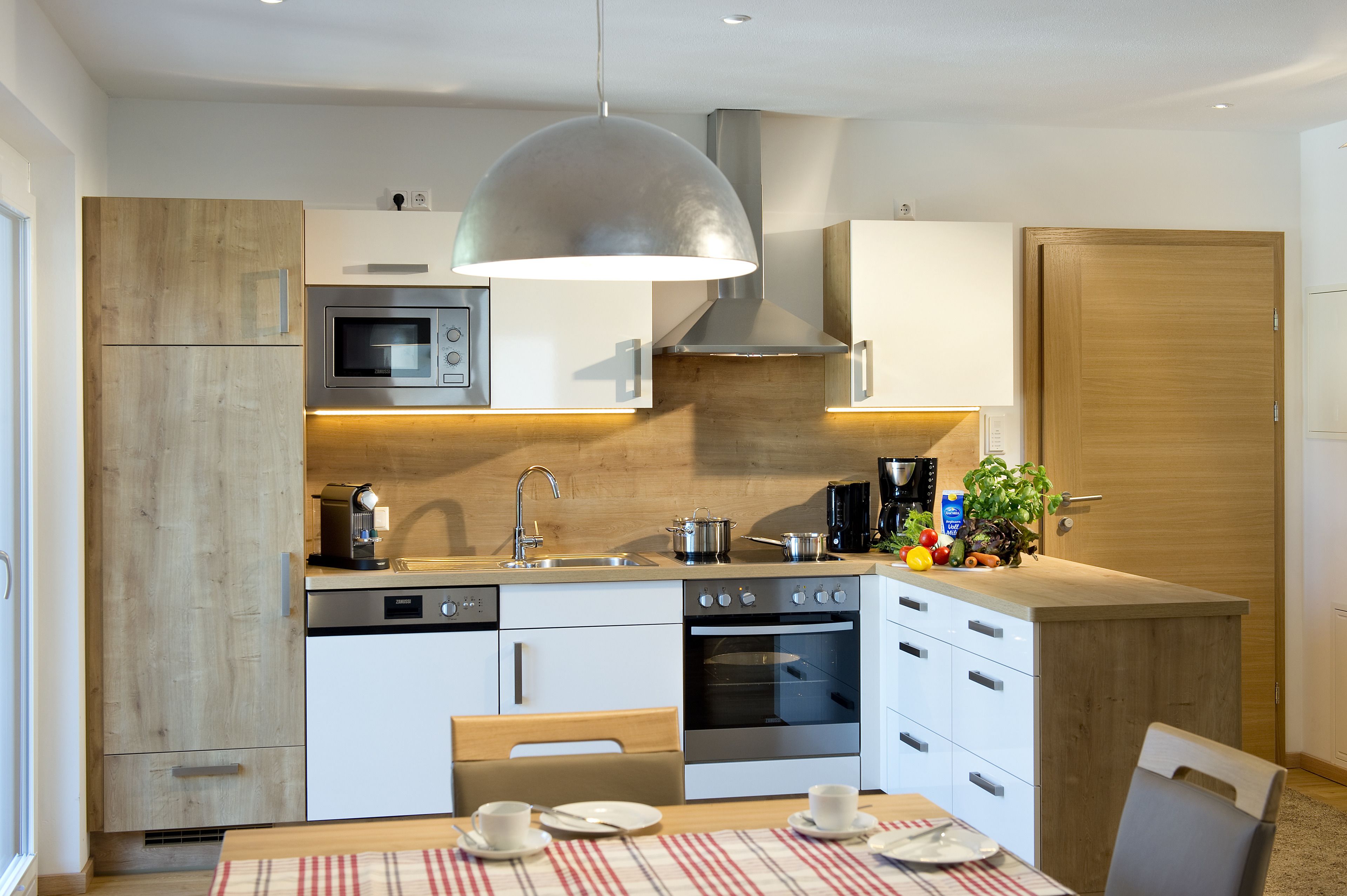 Una cocina moderna con microondas, estufa y horno integrados. Hay un fregadero con grifo, una cafetera y una planta en la encimera.