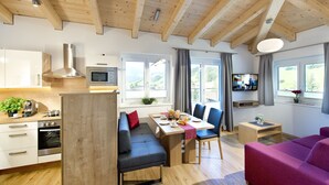 A modern kitchen with a built-in microwave, a dining area with a table set for two, and a cozy seating area with a sofa and a chair. - Dorfjuwel Appartements (Wildschönau)