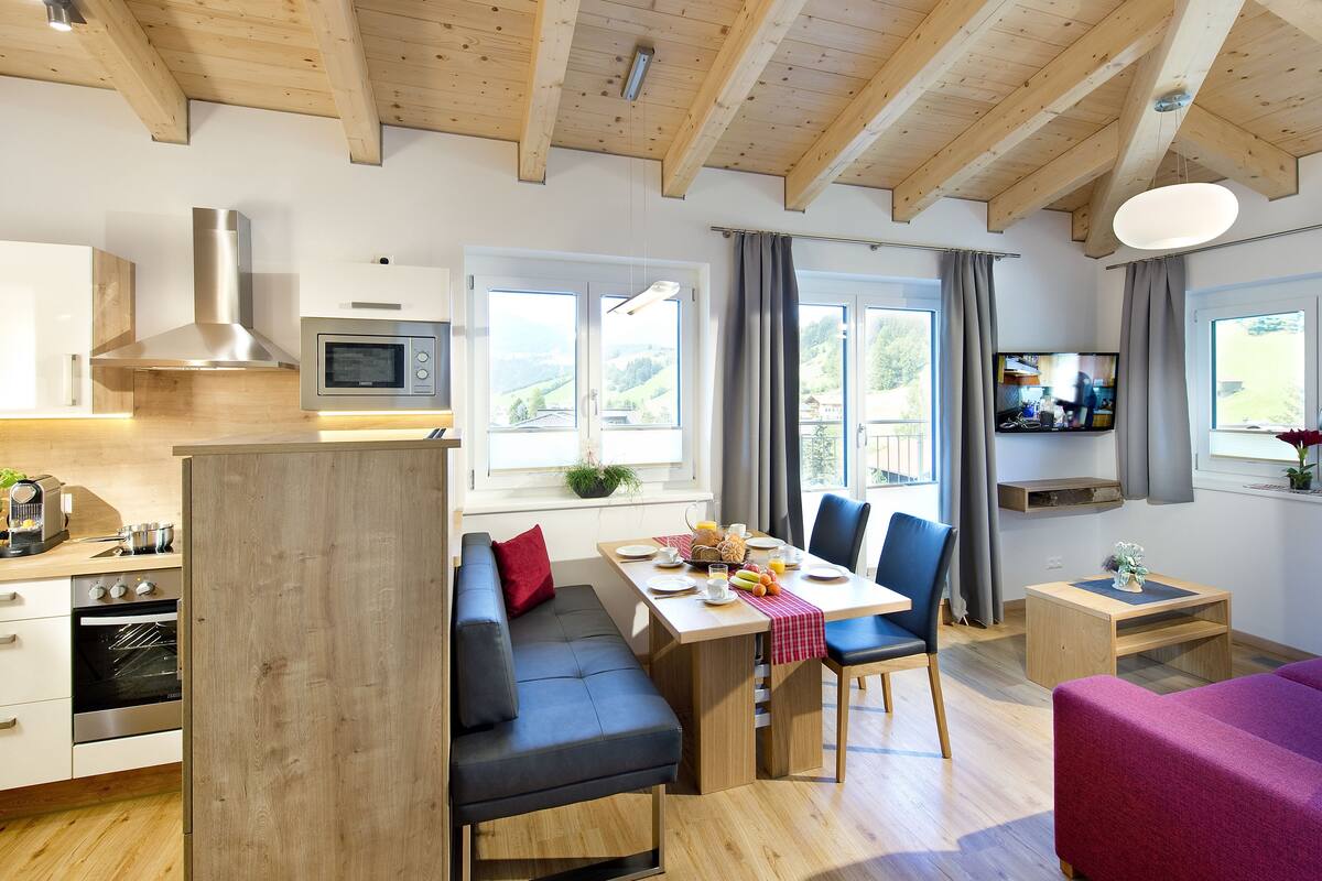 A modern kitchen with a built-in microwave, a dining area with a table set for two, and a cozy seating area with a sofa and a chair.