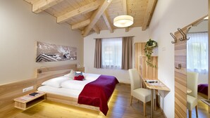 A modern bedroom with a wooden ceiling, a bed with a red blanket, a bedside table, a chair, a desk, and a mirror. - Dorfjuwel Appartements (Wildschönau)
