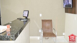 Una reception hotel con un monitor per computer, una tastiera e un telefono. Di fronte al banco, una sedia in vimini e una telecamera di sicurezza montata sulla parete.