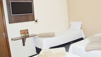 Quarto de hotel com duas camas de solteiro, uma televisão presa à parede, uma pequena prateleira com um menu e uma porta com puxador.