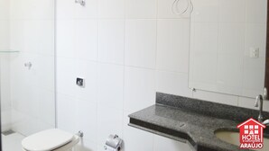 Un bagno con piastrelle bianche, un water, un lavabo con piano in granito e una doccia.