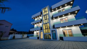 A modern multi-story building with a flat roof, large windows, and a paved courtyard. - Boutique Apartments Blitz (Bibinje)