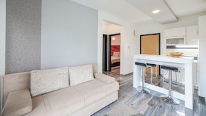 A modern living room with a beige sofa, a white coffee table, and a kitchen area with a white countertop and bar stools. - Boutique Apartments Blitz (Bibinje)