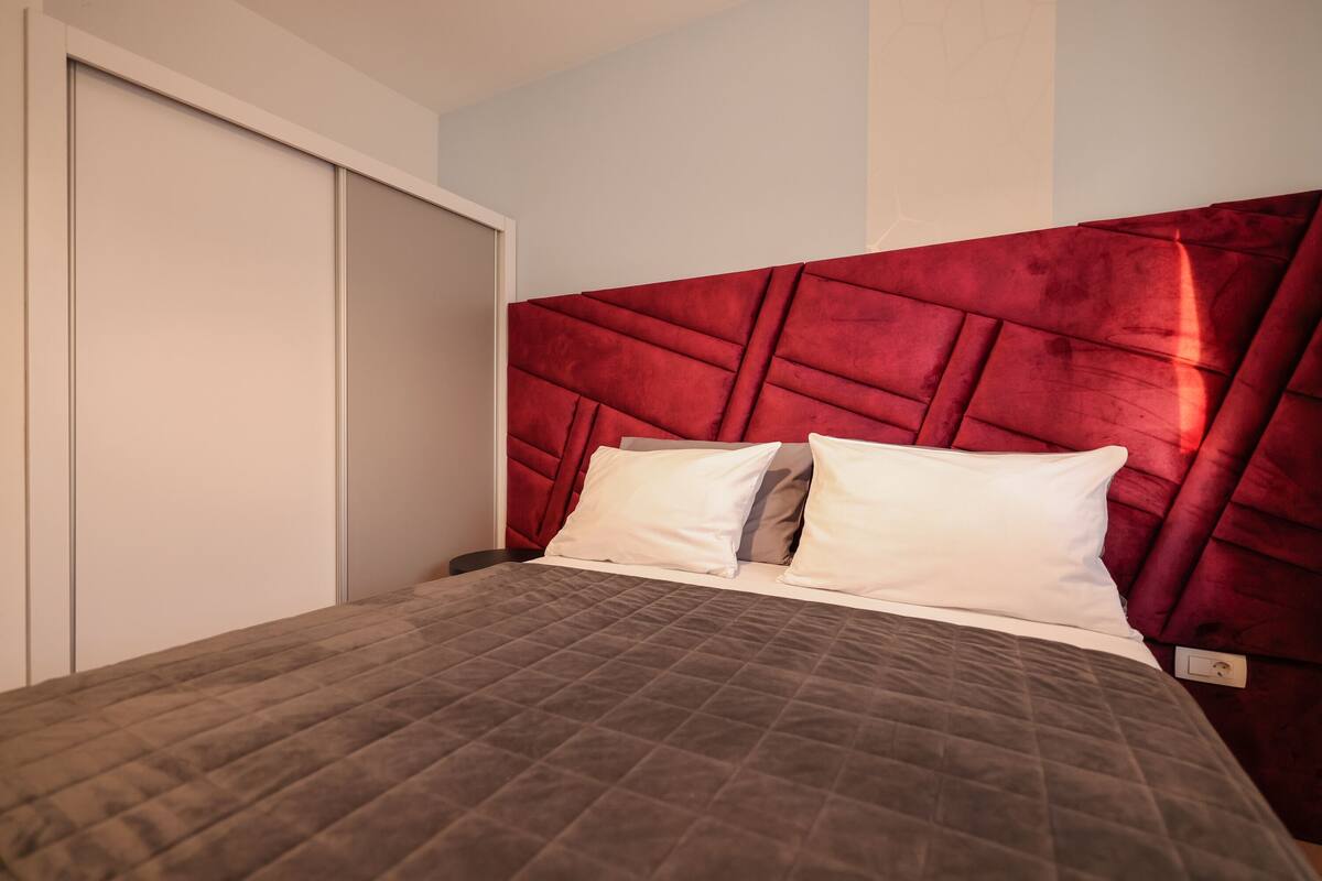 Una cama con cabecera acolchada, una puerta cerrada y una pared con diseño geométrico.
