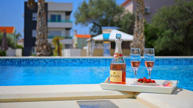 A bottle of RÖMER wine, two glasses, and a tray with strawberries and a rose petal by a poolside. - Boutique Apartments Blitz (Bibinje)