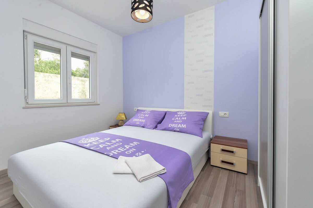 Un dormitorio con una cama, una mesita de noche, una lámpara de pared y una ventana.