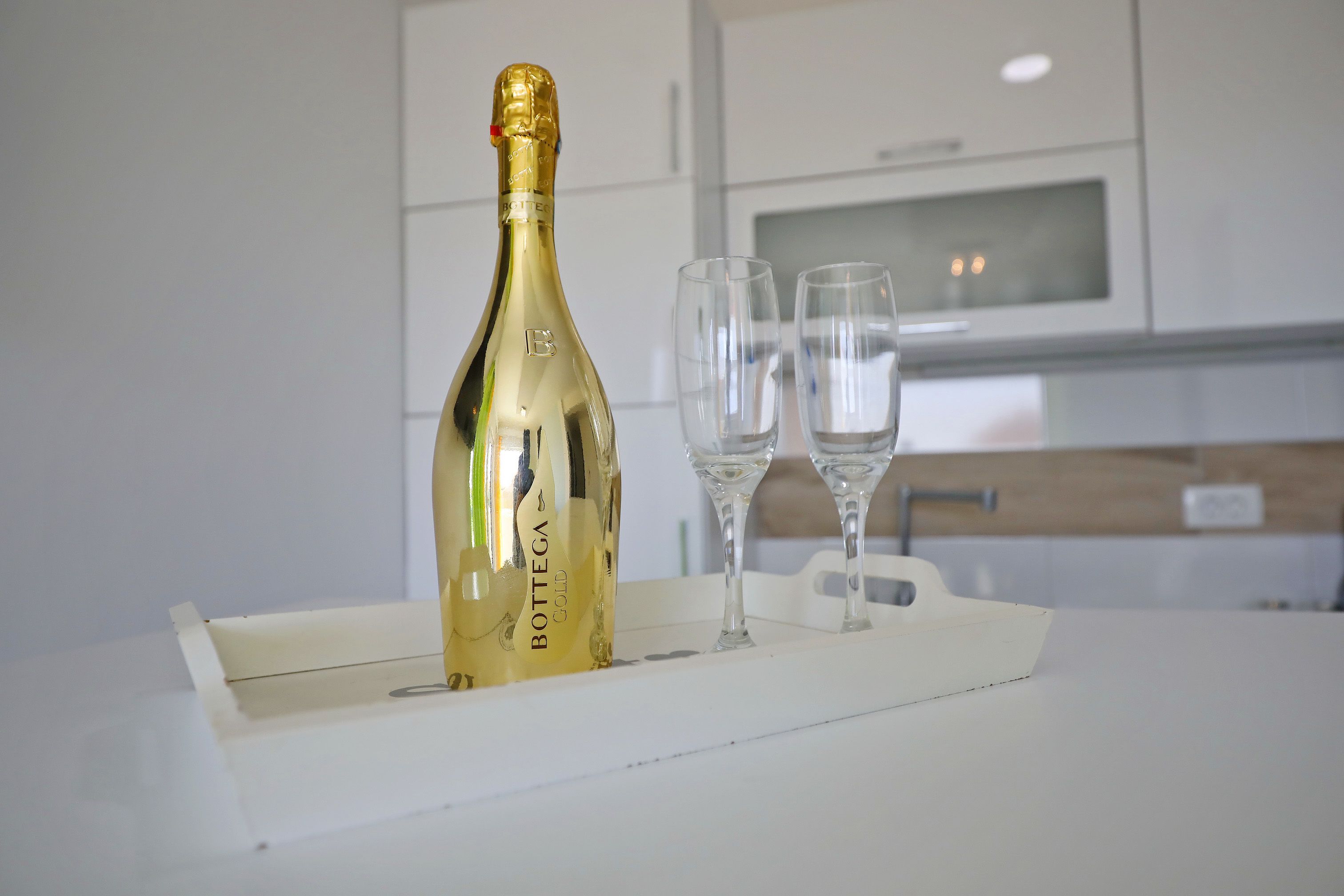 Een fles Bottega Gold champagne en twee glazen op een witte serveerplank in een moderne keuken.